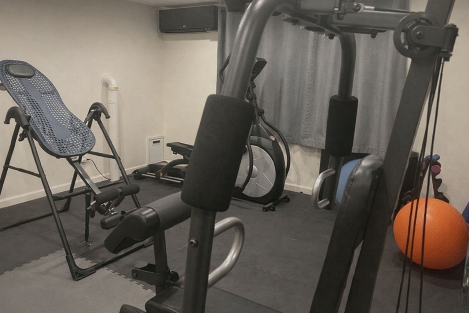 Utrustning i ett hemmagym med en inverterad bänk, motionscykel och vikter.